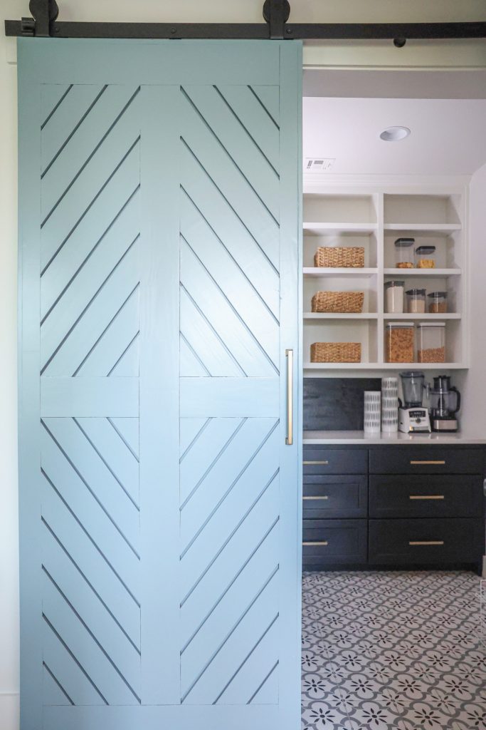 Luxury interior design by Kirkendall Design in Tulsa, OK showing a barn door painted Benjamin Moore’s Courtland Blue opening to a walk-in pantry with beautiful tile and ample storage.
