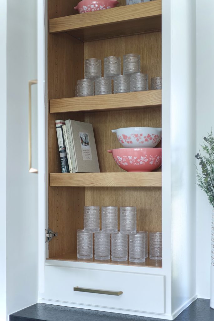 Luxury kitchen design by Kirkendall Design in Tulsa, OK featuring illuminated cabinet shelves displaying a collection of heirloom dishes, artfully arranged between cabinetry mullions.