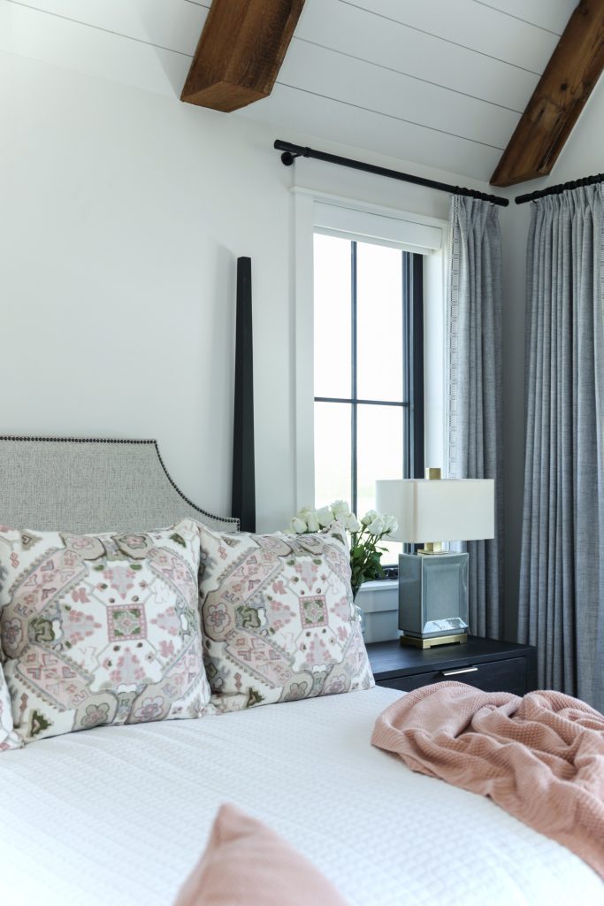 Luxury interior design by Kirkendall Design in Tulsa, OK showing a primary bedroom with an oversized four-poster bed, seating area, remote-controlled shades, blackout curtains, and patterned accents in blue, white, and peachy pink.