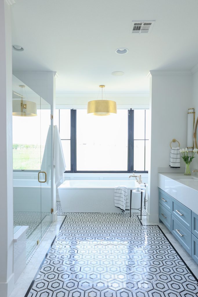 Luxury interior design by Kirkendall Design in Tulsa, OK featuring a spa-like primary bathroom with a large soaking tub, walk-in shower, double vanities, and a floor with a stone hexagon pattern and Carrara subway border.