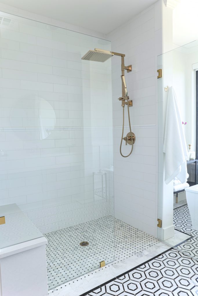 Luxury interior design by Kirkendall Design in Tulsa, OK featuring a spa-like primary bathroom with a large soaking tub, walk-in shower, double vanities, and a floor with a stone hexagon pattern and Carrara subway border.