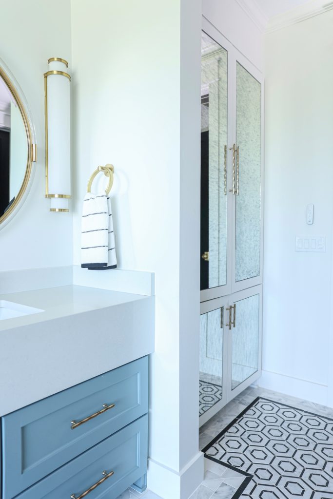 Luxury interior design by Kirkendall Design in Tulsa, OK featuring a spa-like primary bathroom with double vanities, a stone hexagon floor with Carrara subway border, and a linen closet with antique mirrored fronts.