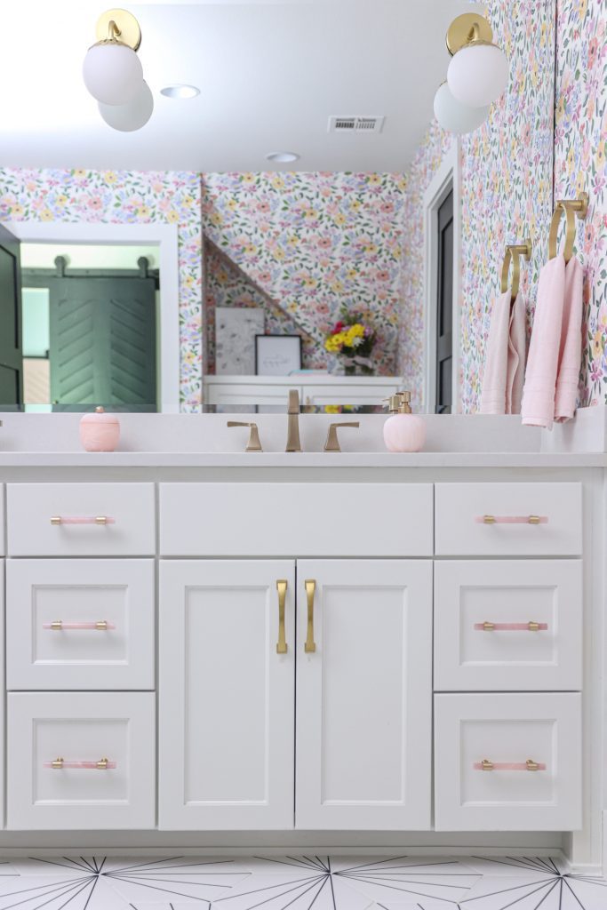 Luxury interior design by Kirkendall Design in Tulsa, OK featuring a girls’ bathroom with bright floral wallpaper, round wall sconces, black-and-white starburst tile, and a white vanity.