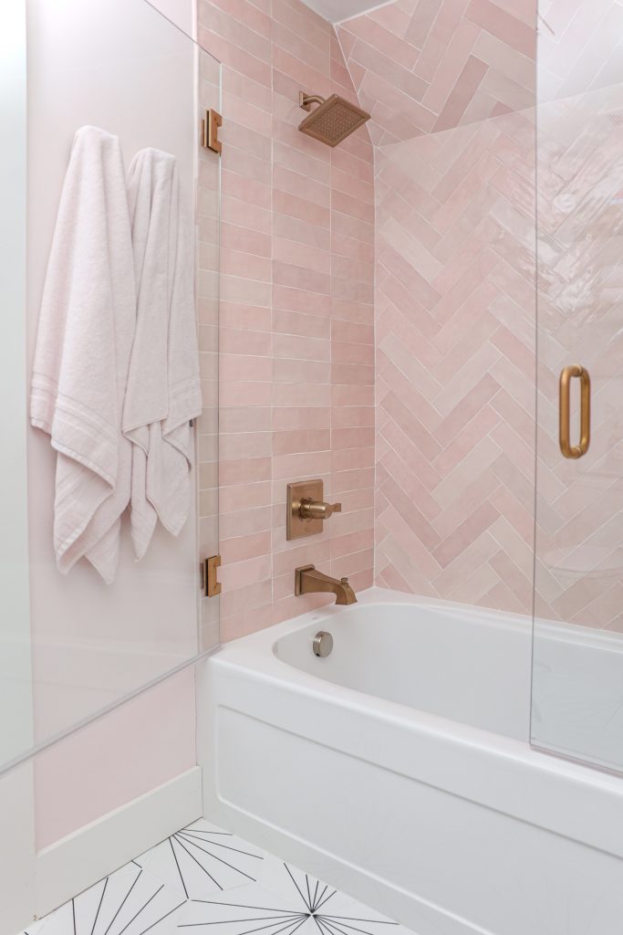 Luxury interior design by Kirkendall Design in Tulsa, OK showing a bathtub with pink tile and dual shower doors above, creating an open and airy bathing space.