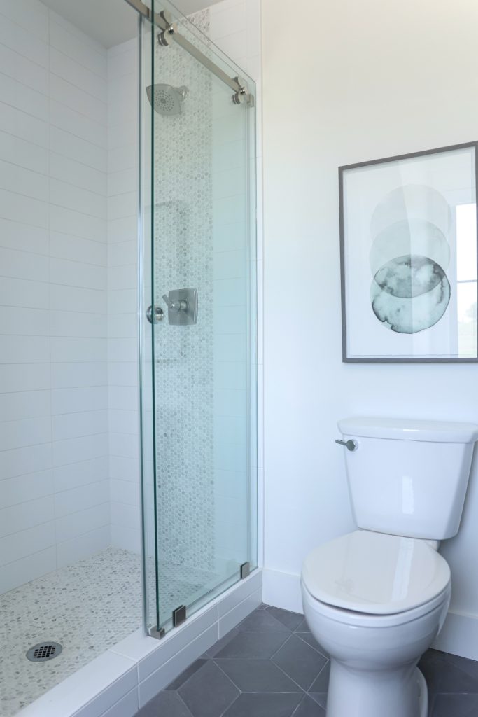 Luxury interior design by Kirkendall Design in Tulsa, OK featuring a boys’ en suite bathroom with a neutral grey palette, mosaic penny tile on the shower floor, and a vertical accent stripe on the shower wall.
