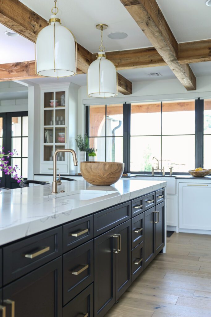 Luxury interior design by Kirkendall Design in Tulsa, OK showcasing a kitchen island with Bianco Statuario Quartz, farmhouse apron sink, Hudson Valley pendant lighting, large windows overlooking the front yard, and custom cabinetry.
