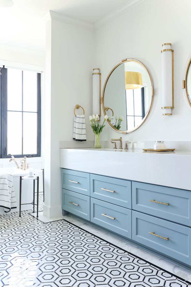 blue bathroom vanity with hexagon bold tile. round gold mirror and gold sconces interior design by Kirkendall Design in Tulsa, OK