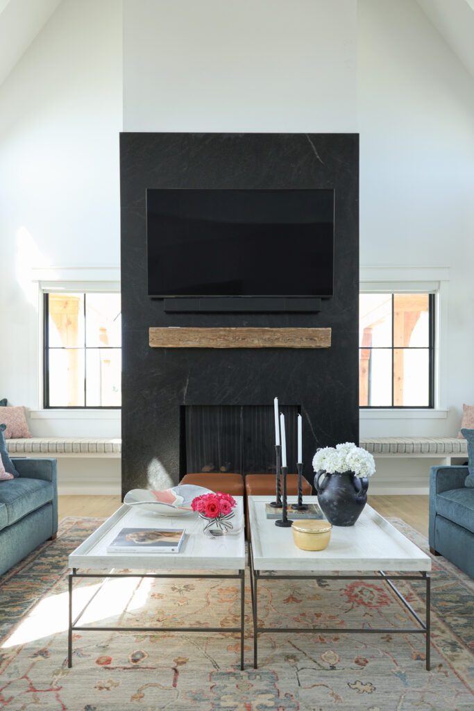 Built-in benches with cushions on either side of a black granite fireplace, framed by tall windows that fill the luxury living room with natural light and provide additional seating for gatherings. Designed by Kirkendall Design in Tulsa OK