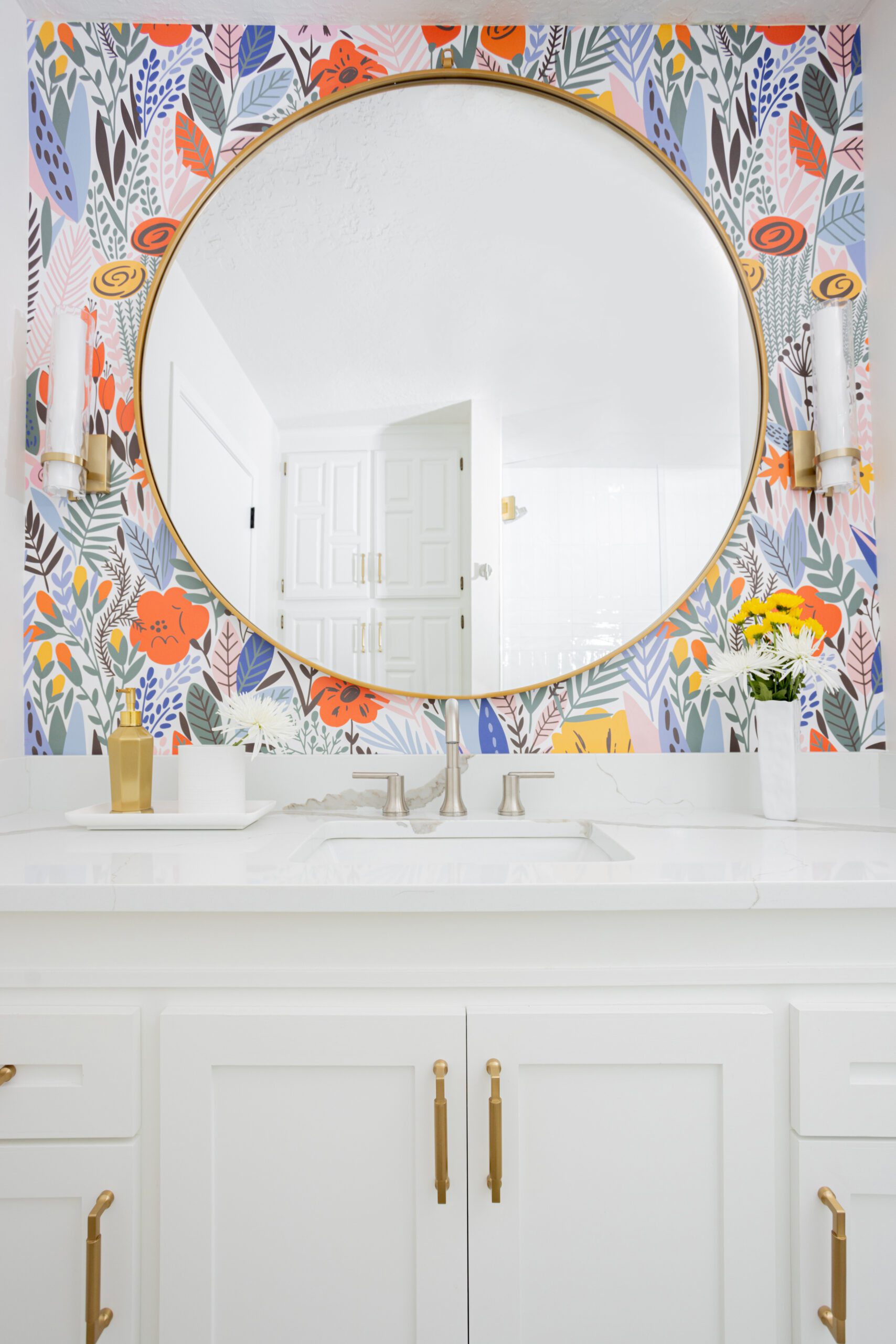 Bright, floral wallpaper in bathroom with white cabinets and gold accents. Design by Kirkendall Design Tulsa OK