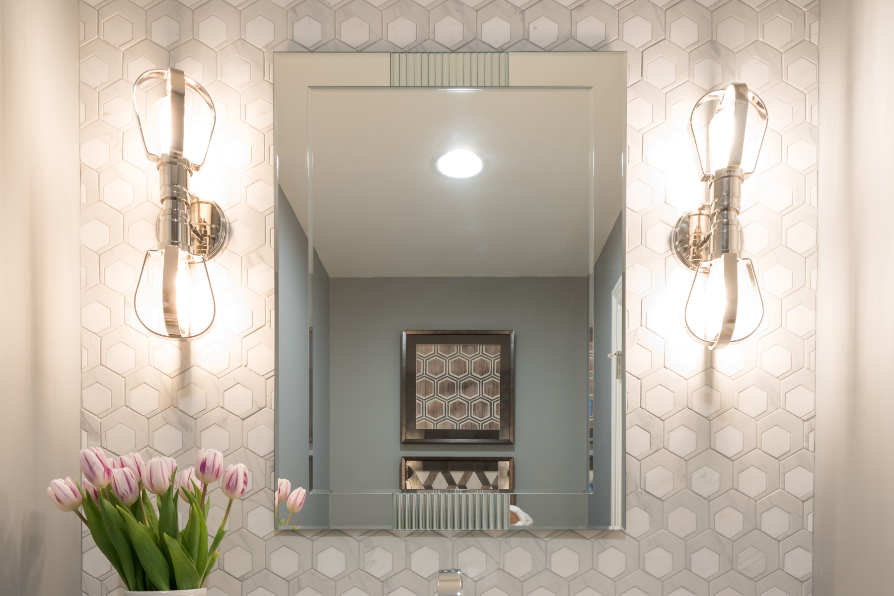 Sconces layered on neutral wallpaper in bathroom above vanity, design by Kirkendall Design