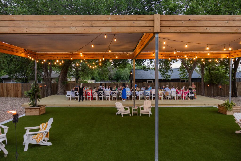 guests eating having family-style dinner outside at The Studio at K|D, plus string lights on the pergola and turf lawn for relaxing