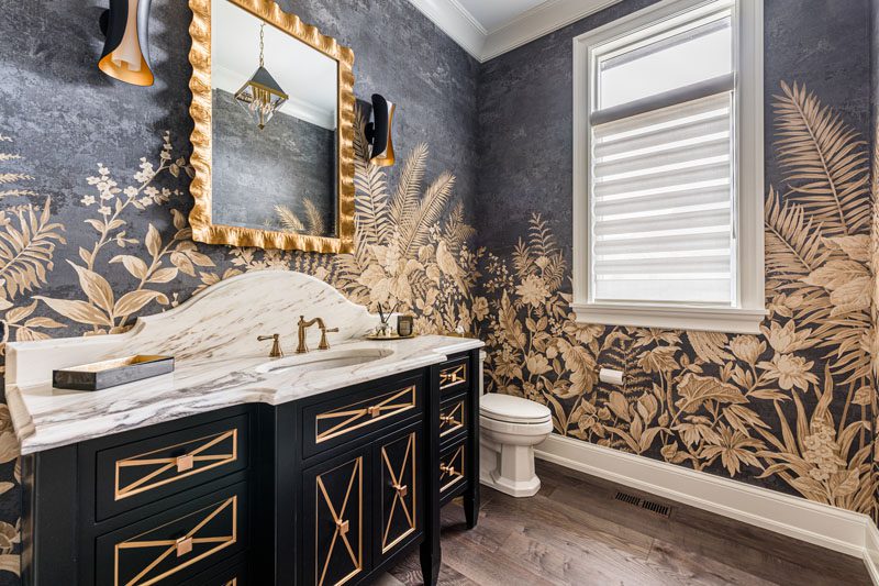 NKBA 2025 award-winning powder bath featuring a curved backsplash, large-scale gold-leaf wallcovering, a black vanity, and gold accents.
