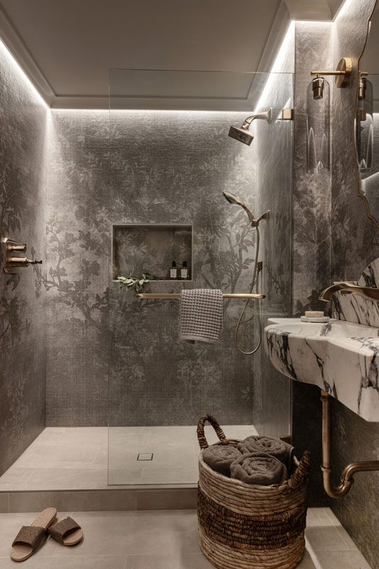 NKBA 2025 award-winning bathroom featuring indirect cove lighting and botanical tree wallcovering that extends from the bathroom walls into the shower.