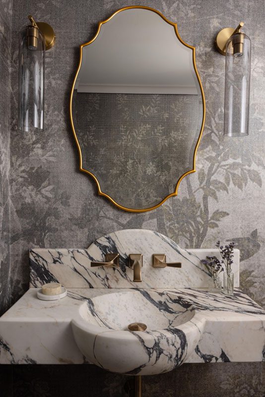 NKBA 2025 award-winning bathroom featuring a botanical wallcovering, ornate gold mirror, curved marble backsplash, and floating vanity.