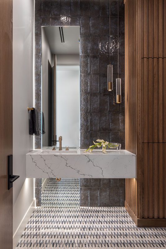 NKBA 2025 award-winning powder bath featuring a teak panel wall, full-height tiled backsplash, and a floating white quartz vanity with black veining.
