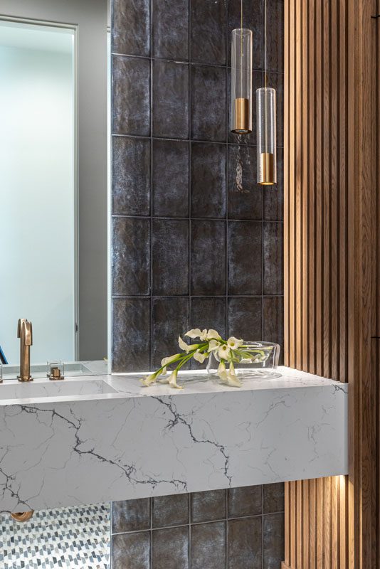 NKBA 2025 award-winning powder bath featuring a teak panel wall, full-height tiled backsplash, and a floating white quartz vanity with black veining.