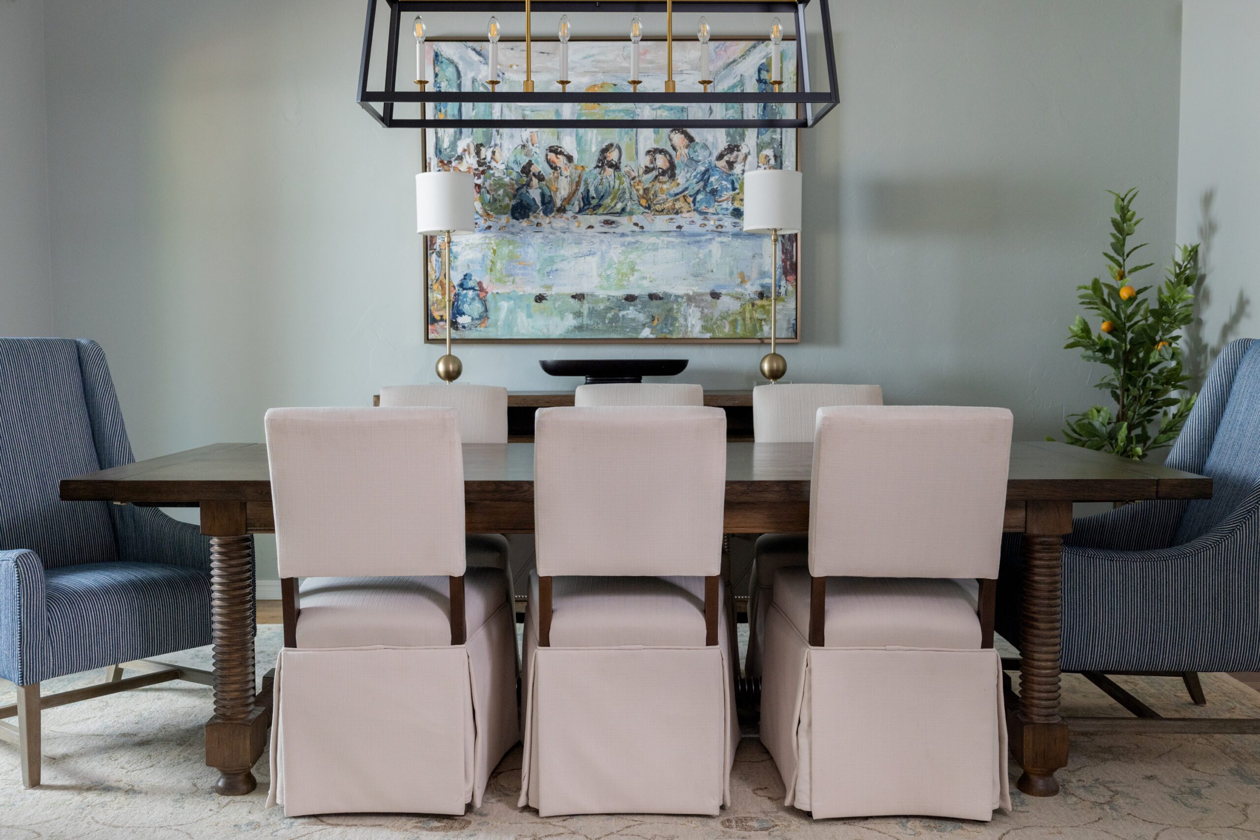 Luxury interior design by Kirkendall Design in Tulsa, OK featuring a refreshed dining room with the clients’ existing table paired with new upholstered chairs, blue striped head chairs for contrast, and reframed artwork that elevates the space.