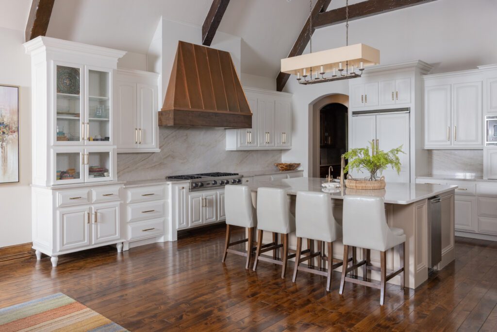 Old-world style transformed by Kirkendall Design, Tulsa, OK into a spacious, modern kitchen with white cabinets, quartzite countertops and backsplash, and a high vaulted ceiling featuring a wood beam.