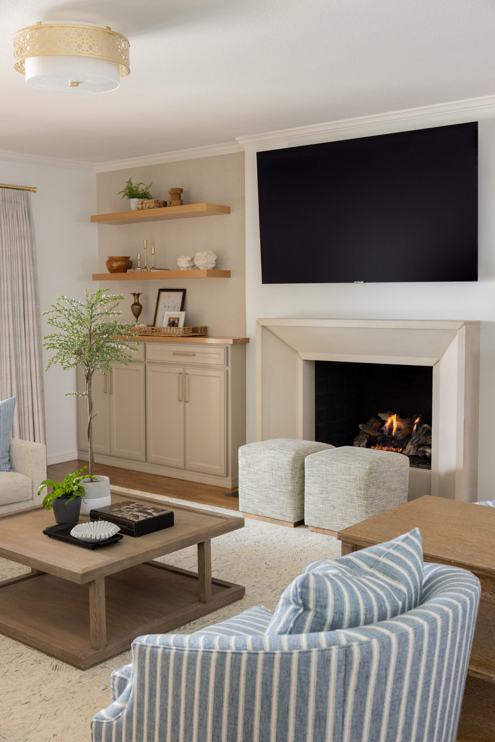 Luxury interior design by Kirkendall Design in Tulsa, OK showing a main-level renovation and full-service interior design living room, picture is the remodeled stone fireplace with custom built-ins, layered seating, and a collected Nancy Meyers–inspired aesthetic in soft blues, greens, and creams.