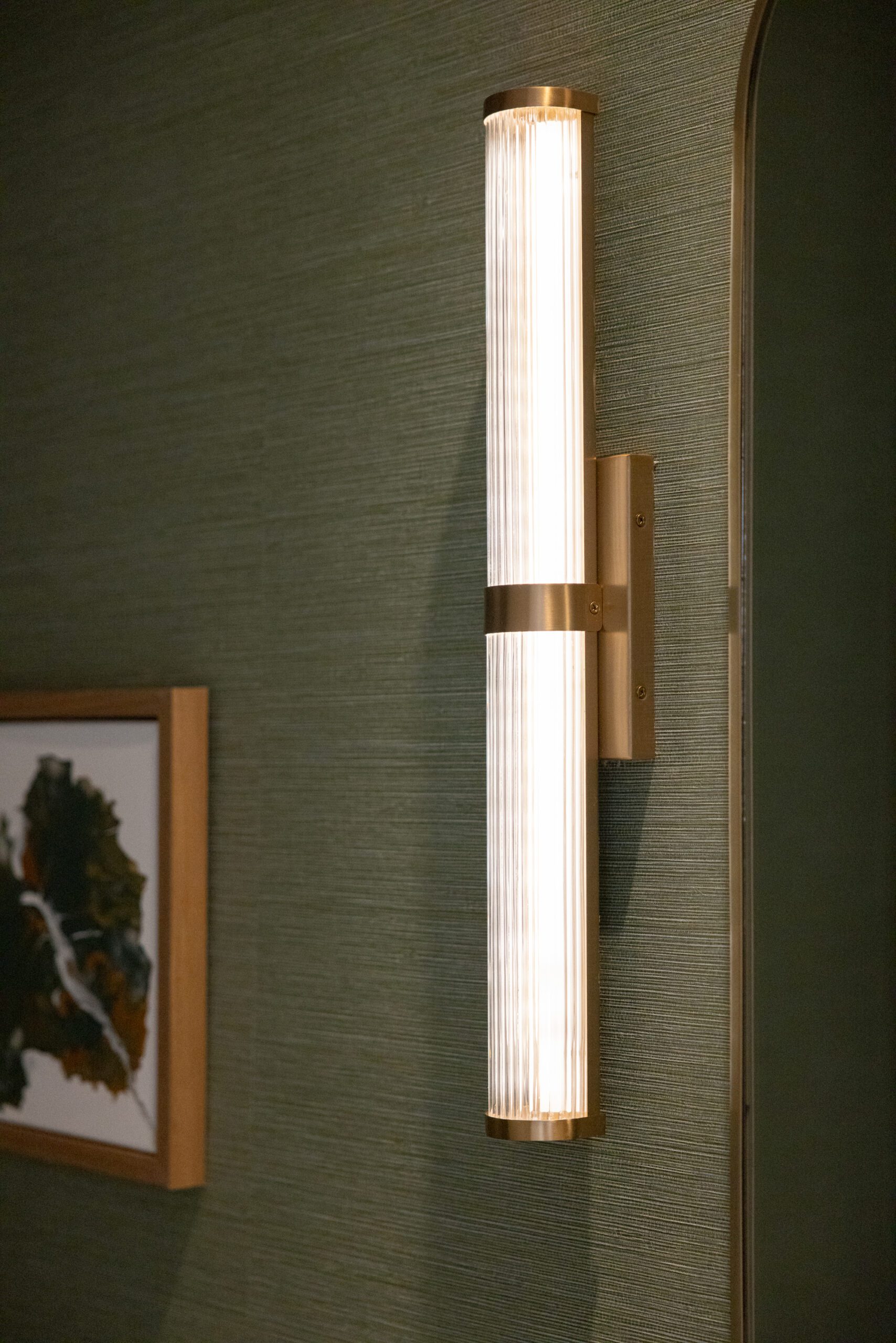 Green wallpaper in bathroom with gold linear wall sconce, interior design by Kirkendall Design