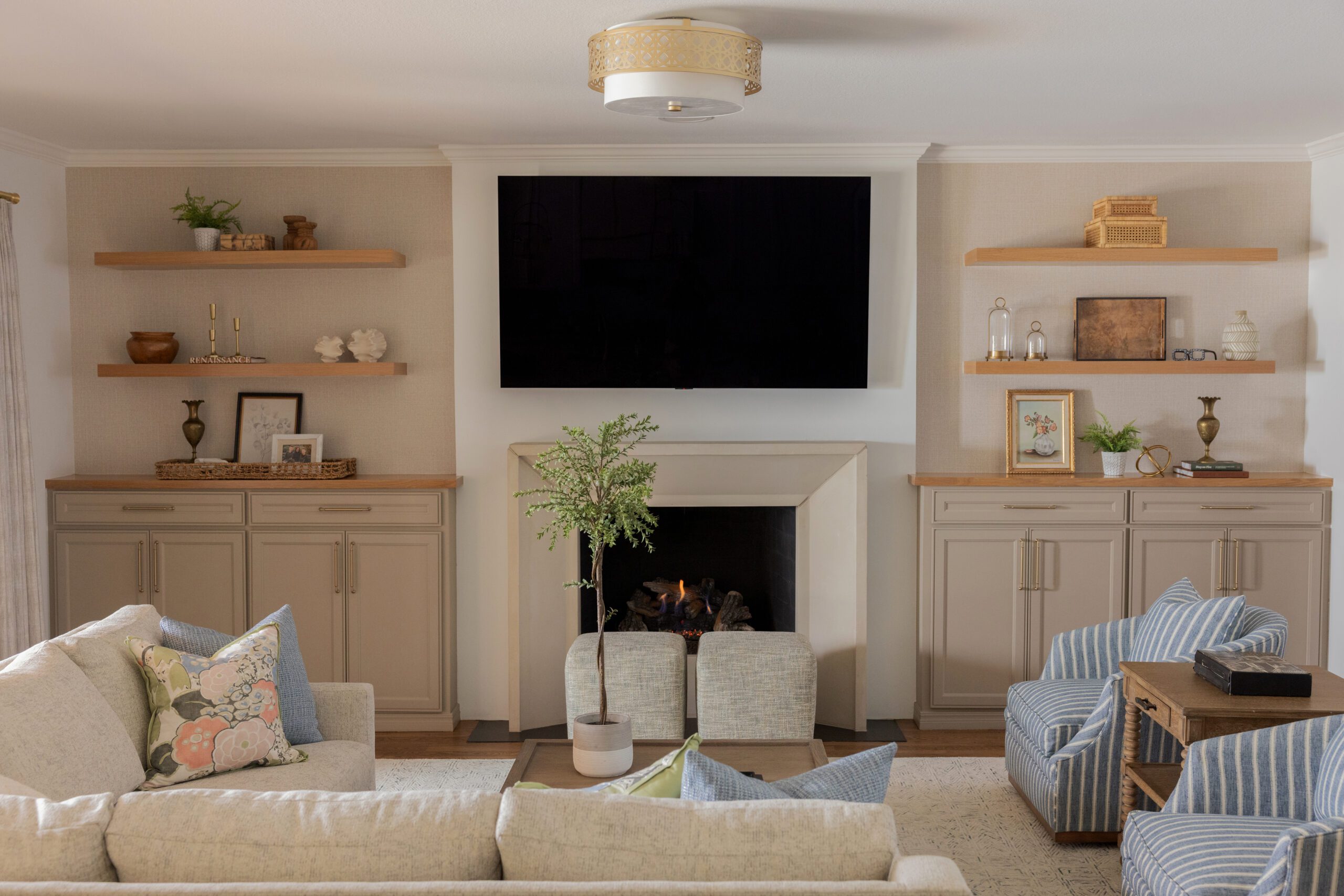 Luxury interior design by Kirkendall Design in Tulsa, OK showing a main-level renovation and full-service interior design living room, viewed from behind the sofa toward a remodeled stone fireplace with custom built-ins, layered seating, and a collected Nancy Meyers–inspired aesthetic in soft blues, greens, and creams.