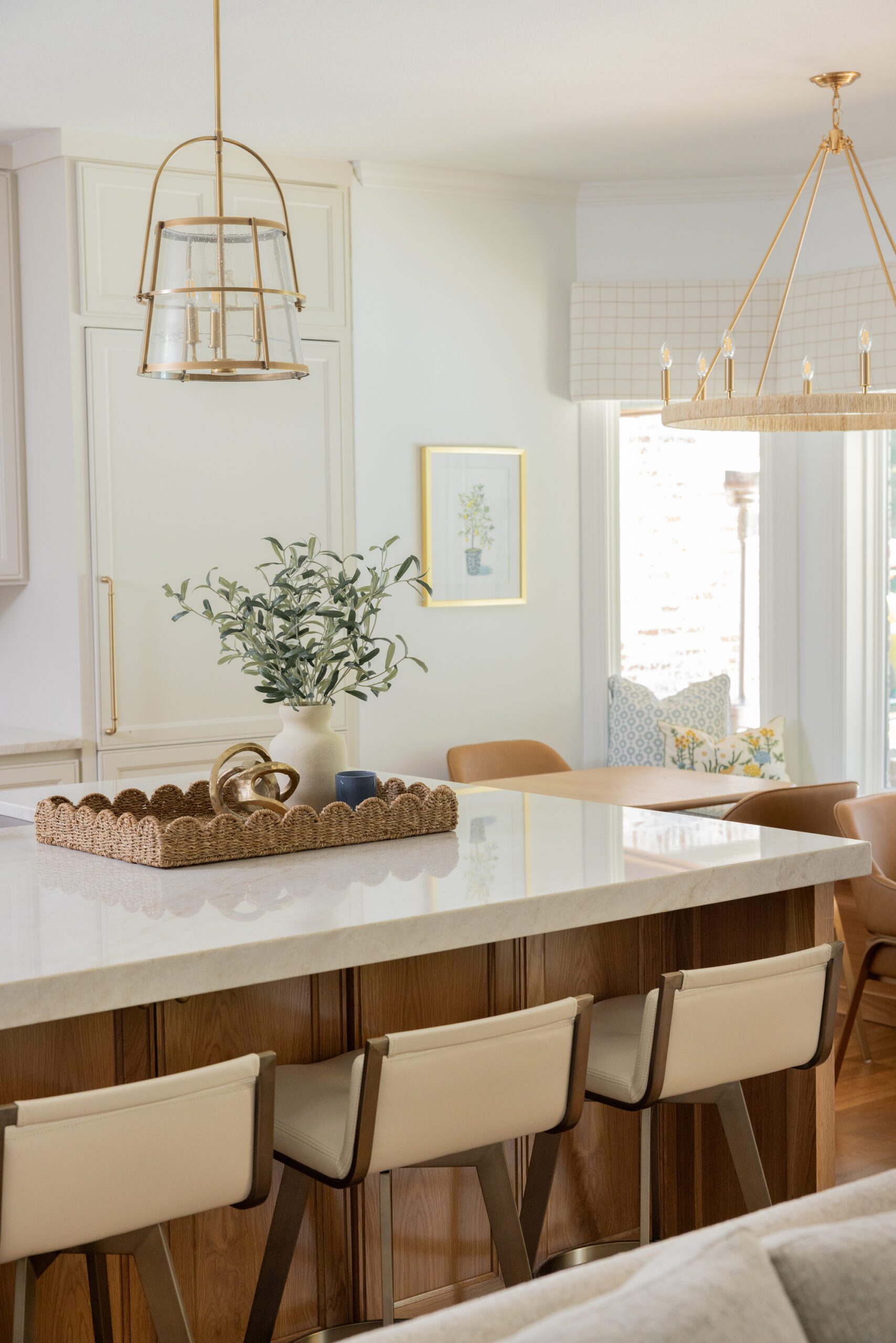 Luxury interior design by Kirkendall Design in Tulsa, OK featuring a kitchen renovation with an open layout, central island in stained weathered oak, soft neutral cabinetry, quartz countertops, classic ceramic tile backsplash, integrated appliances, and a custom hood with satin brass detailing.