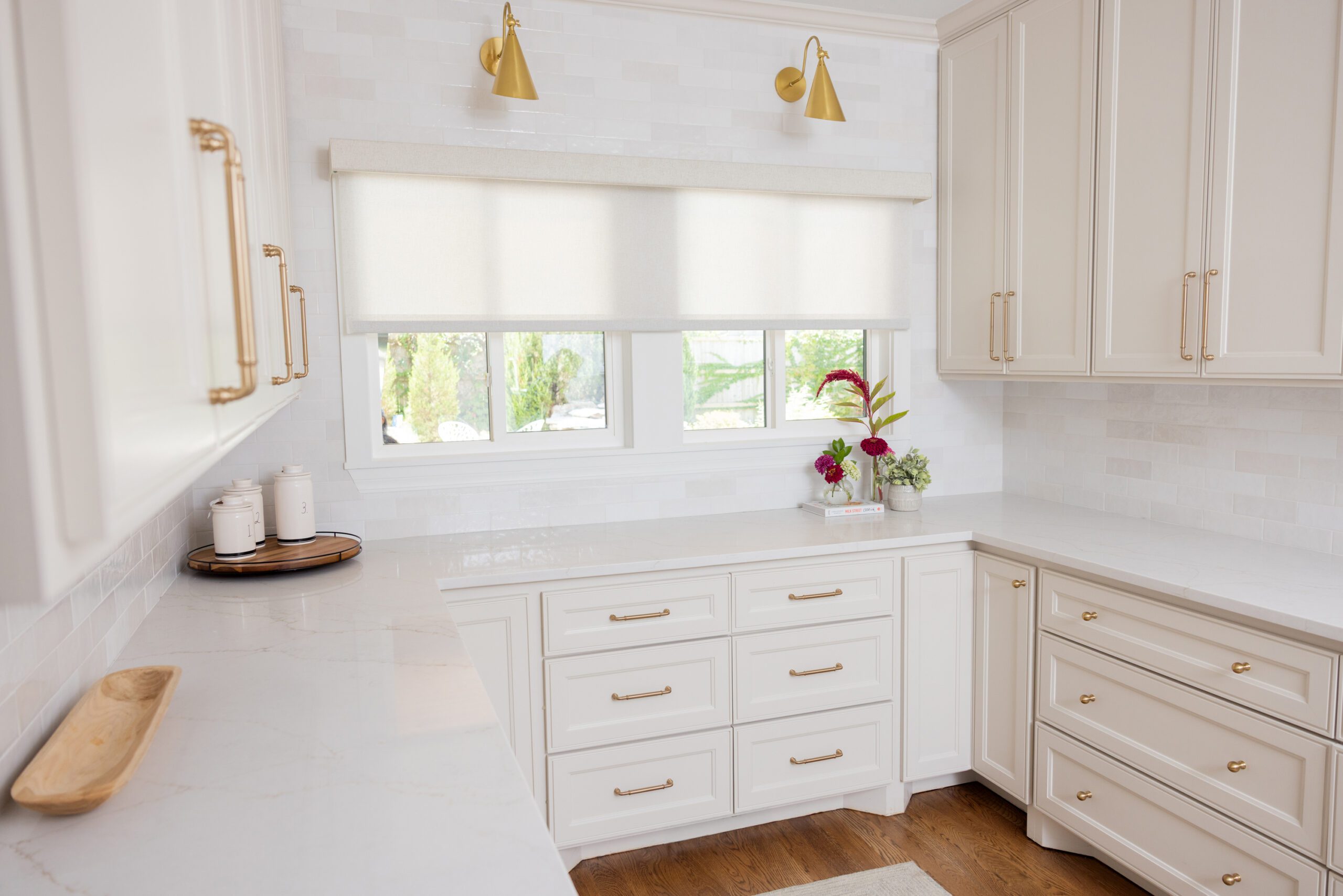 Luxury interior design by Kirkendall Design in Tulsa, OK featuring a dedicated scullery with ample storage, neutral cabinetry, a prep sink, classic two-tone subway tile backsplash, brass hardware and sconces, and a window that fills the space with natural light.