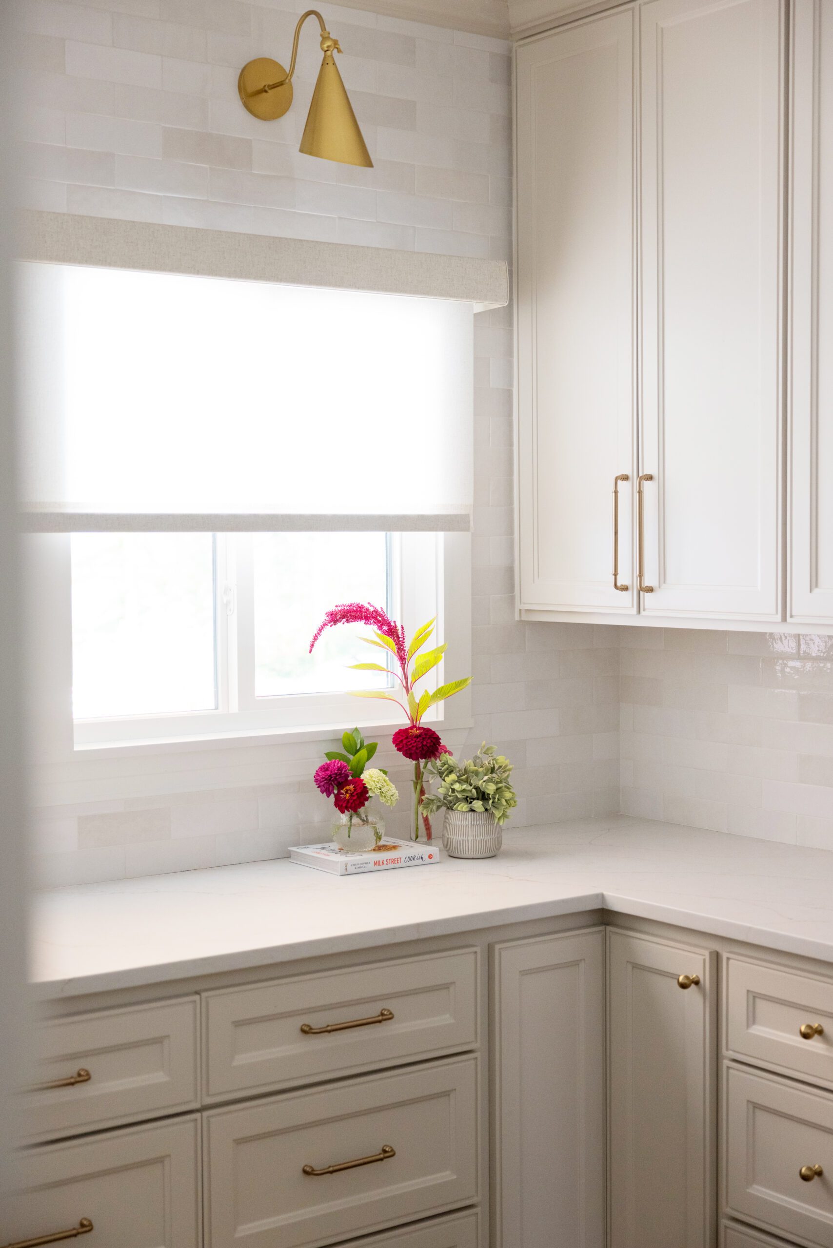Luxury interior design by Kirkendall Design in Tulsa, OK featuring a dedicated scullery with ample storage, neutral cabinetry, a prep sink, classic two-tone subway tile backsplash, brass hardware and sconces, and a window that fills the space with natural light.