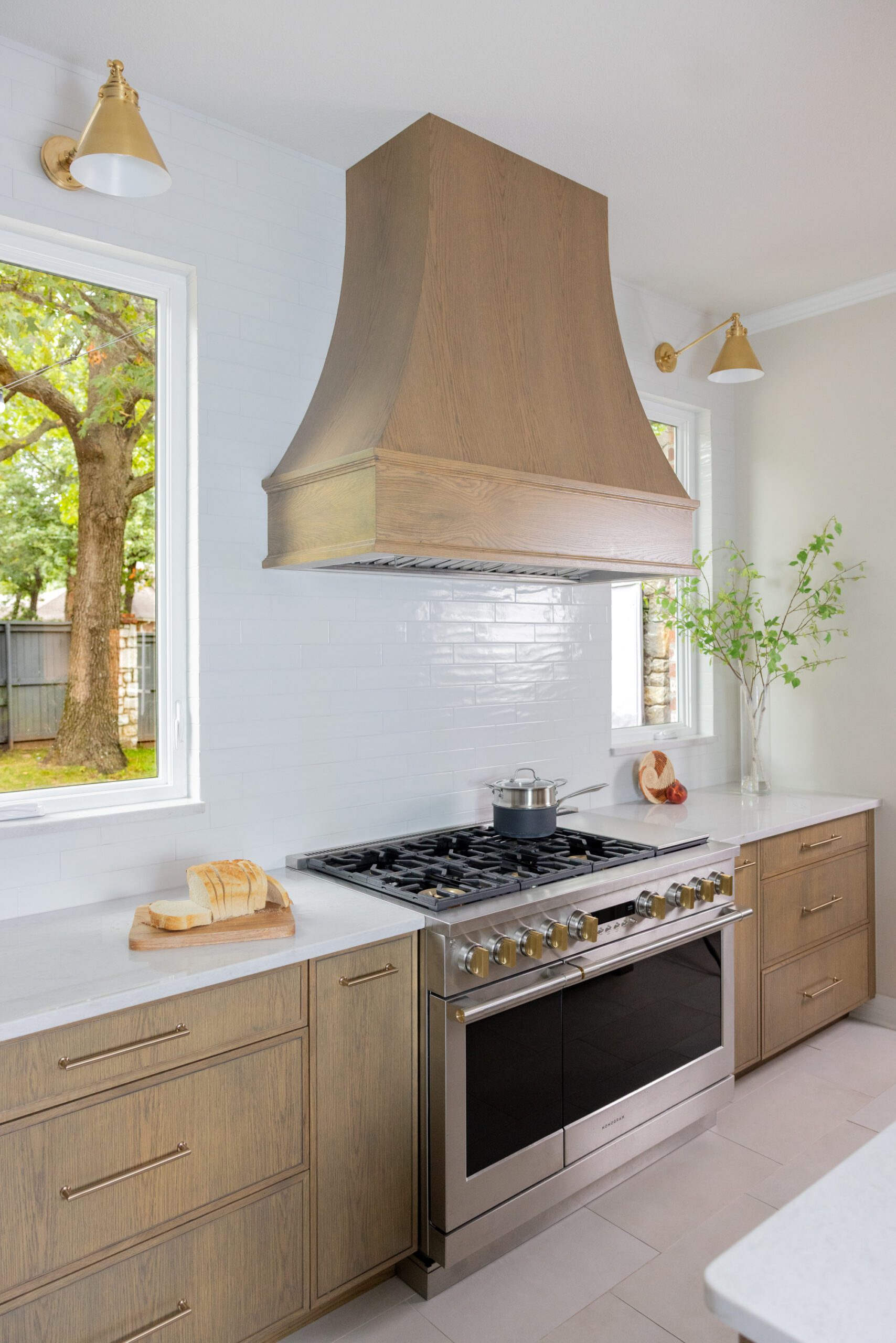 Luxury kitchen range in a Tulsa kitchen renovation featuring a GE Monogram Range, full-height tile backsplash, custom oak hood, and designer sconces.