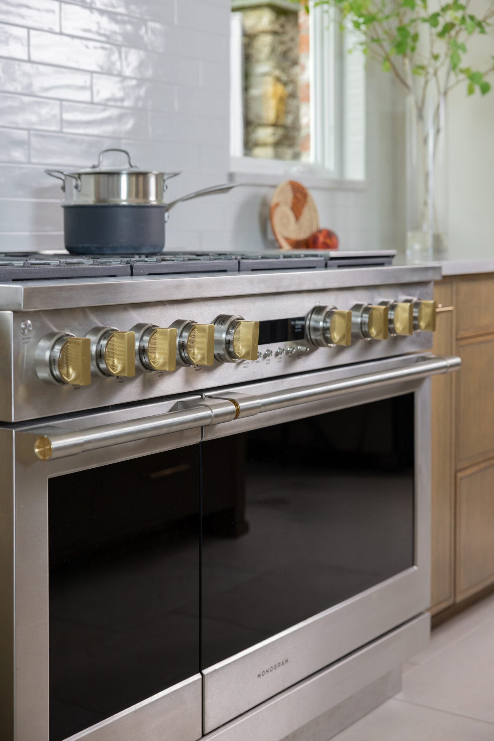 Luxury kitchen range in a Tulsa kitchen renovation featuring a GE Monogram Range, full-height tile backsplash, custom oak hood, and designer sconces.