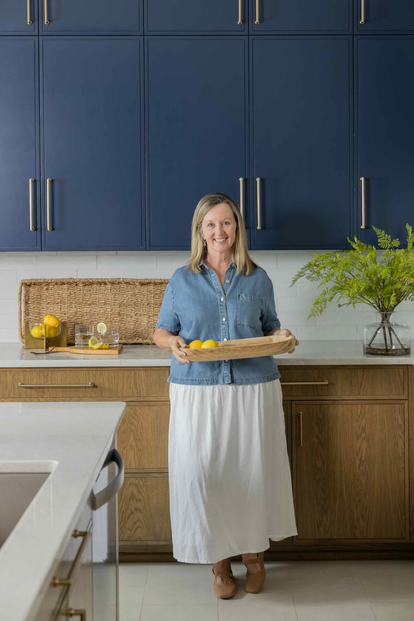Kirkendall Design owner standing in a custom Tulsa kitchen renovation featuring two-tone cabinetry with stained lower cabinets, deep blue upper cabinets, and a large island.