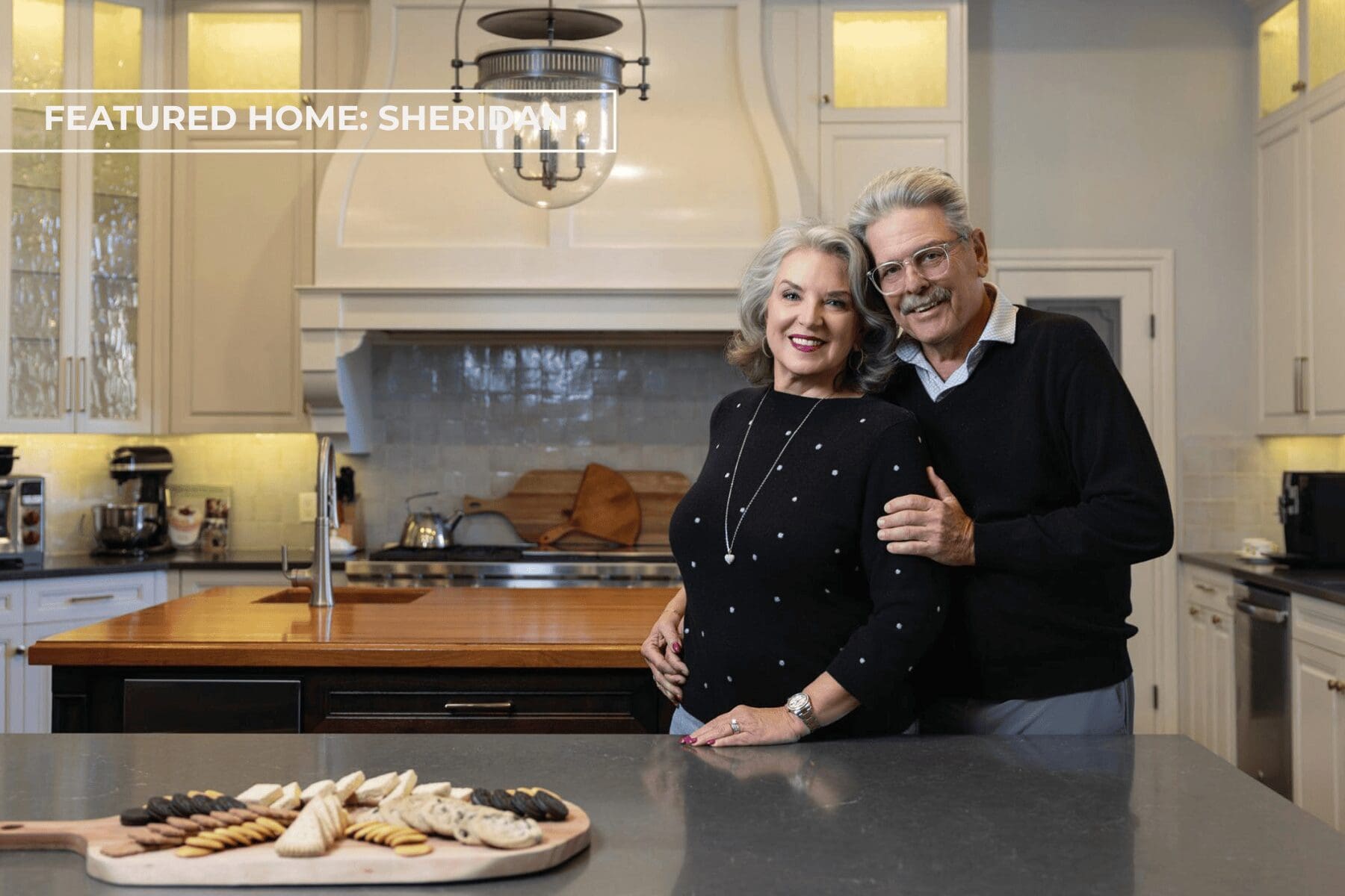 Bernie and Christine Sheridan standing in their luxury kitchen renovation inside their multigenerational Tulsa home designed by Kirkendall Design, featuring custom cabinetry, layered textures, and collected artwork inspired by their travels throughout Asia.