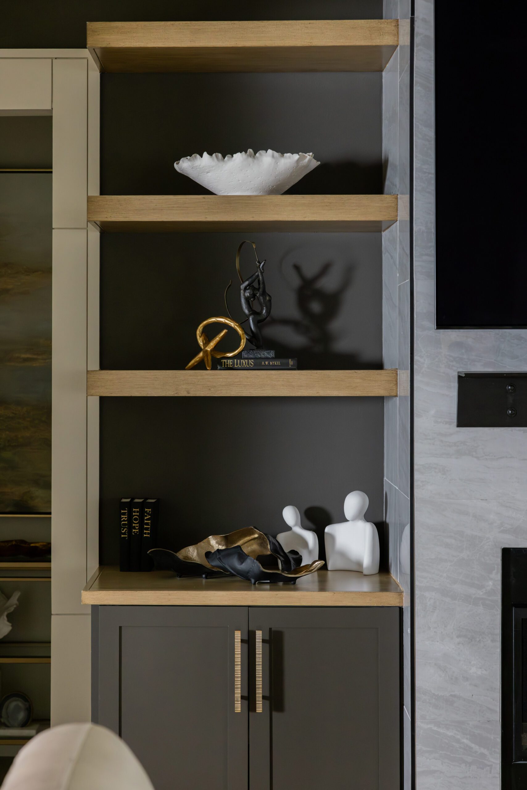 Living room styling detail featuring custom floating shelves beside the fireplace with layered decor and warm wood finishes in a Tulsa new construction home, designed by Kirkendall Design