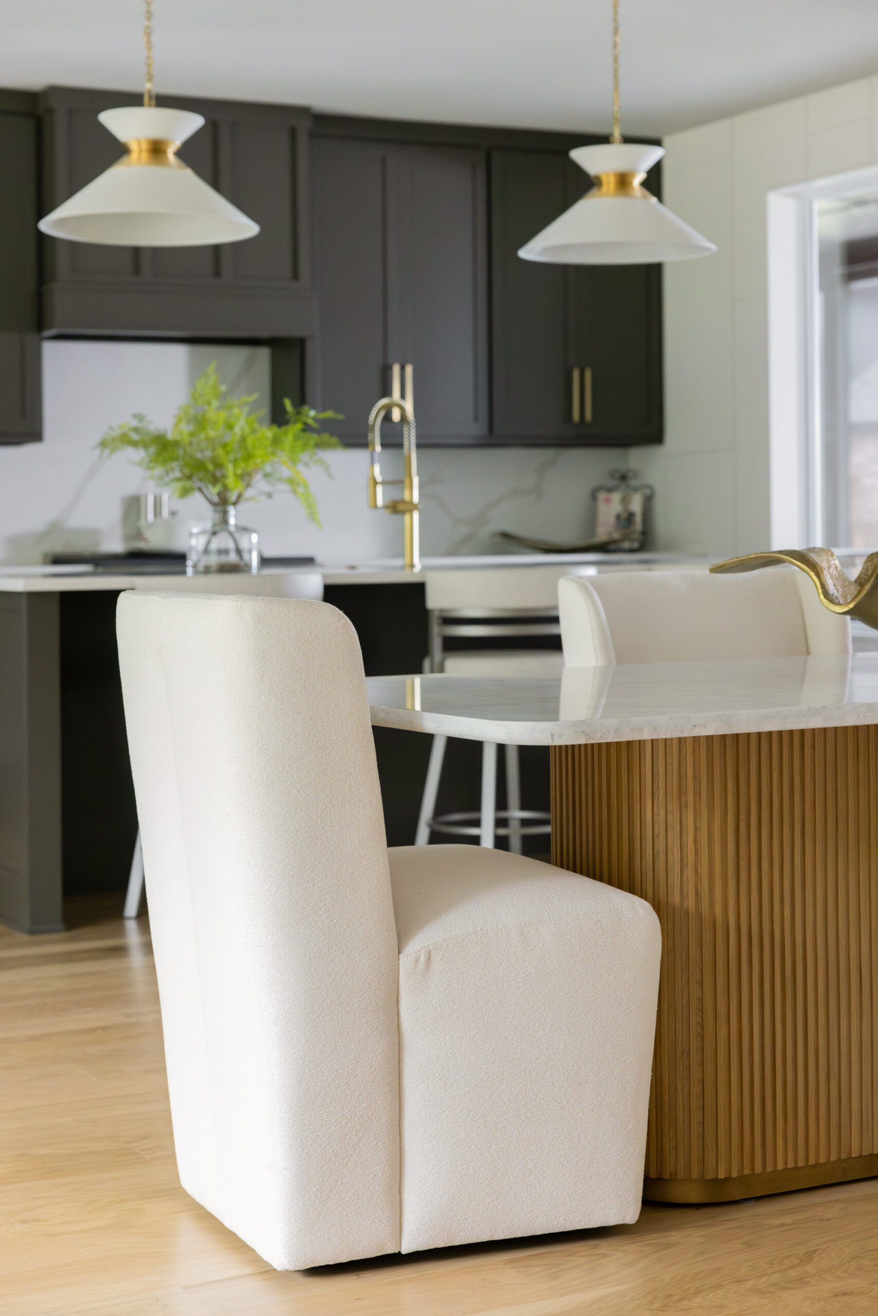 Luxury dining room design in a Tulsa new construction home featuring a modern wingback cream dining chair, elegant table, and warm chocolate brown kitchen cabinetry