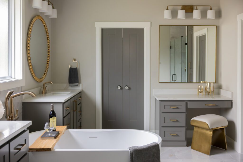 Primary bathroom in a new construction home in Tulsa, updated by Tulsa interior design firm Kirkendall Design with painted vanity cabinets, a custom dressing vanity, and gold hardware details that bring warmth and character.