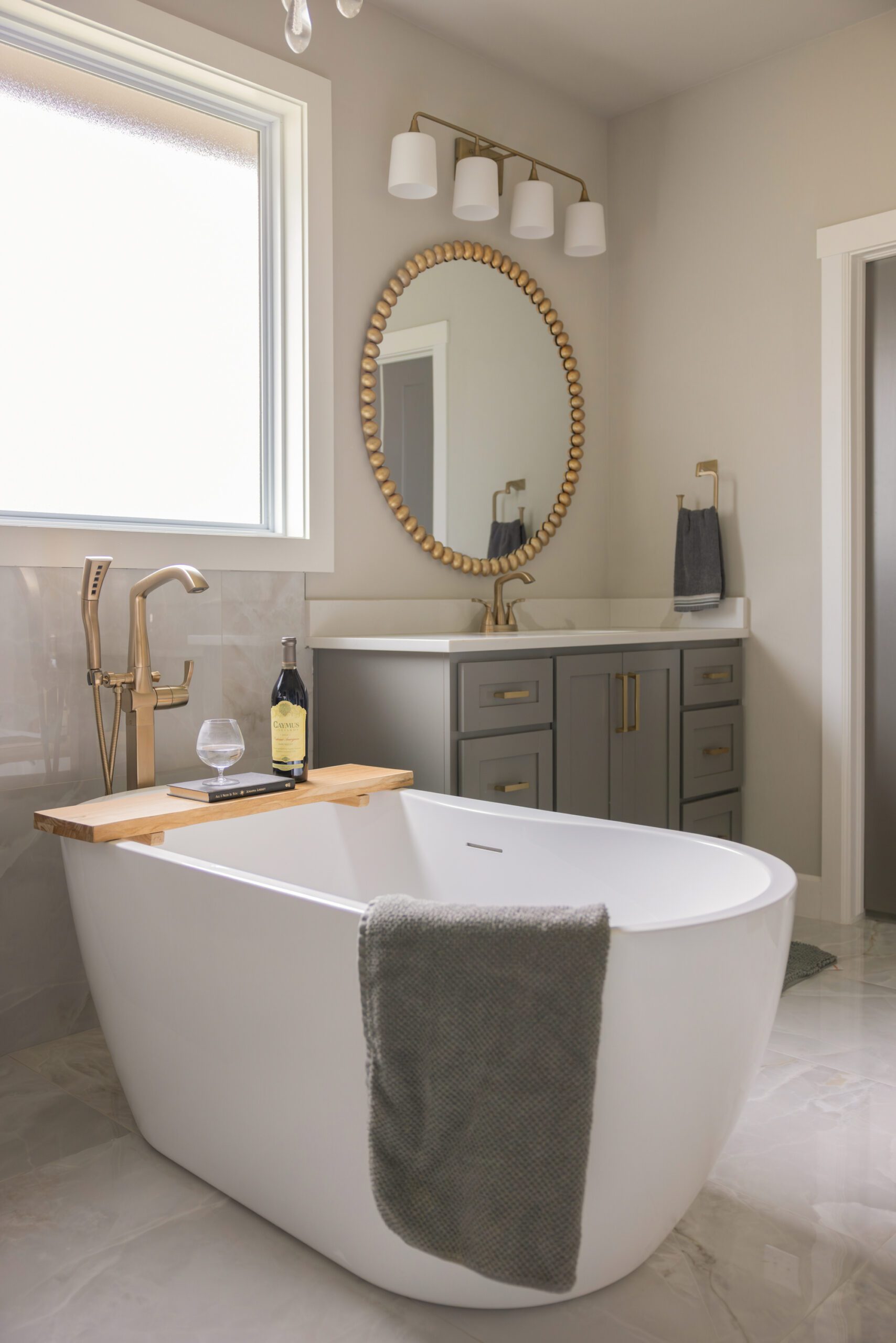 After batrhoom renovation showing a freestanding tub with gold faucet and sprayer, paired with a newly painted dark vanity and gold mirror—part of a Tulsa interior design update bringing softness and personality to a new construction bathroom.