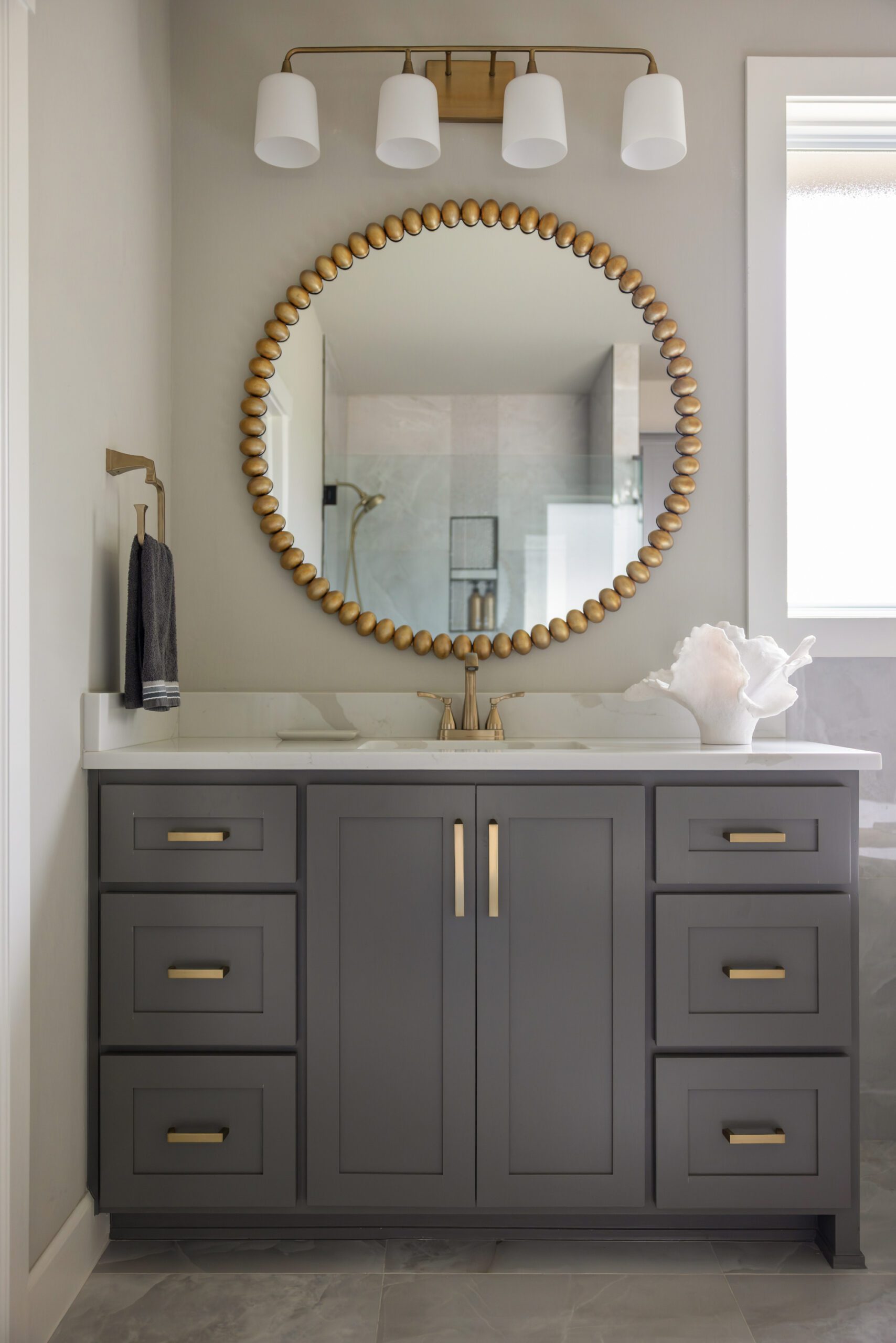 Head-on view of the primary vanity in this Tulsa new construction home, now transformed with dark painted cabinetry, a round gold mirror, and a modern four-light sconce to create depth, personality, and balance.