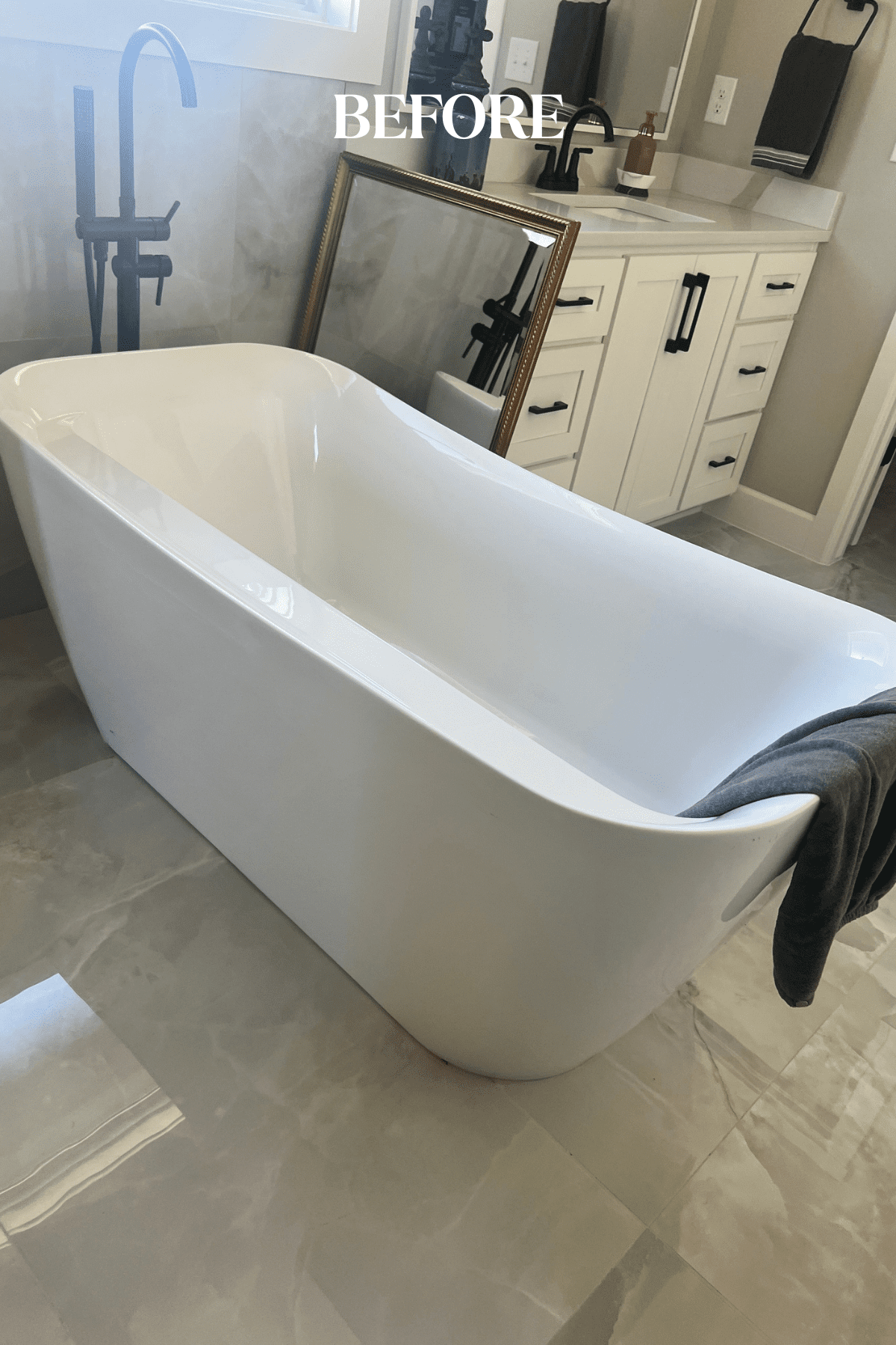 Before image of the new build primary bathroom in Tulsa featuring a stark black-and-white palette with a freestanding tub, black hardware, and white cabinetry that felt unfinished and lacked the personality of a fully designed space.
