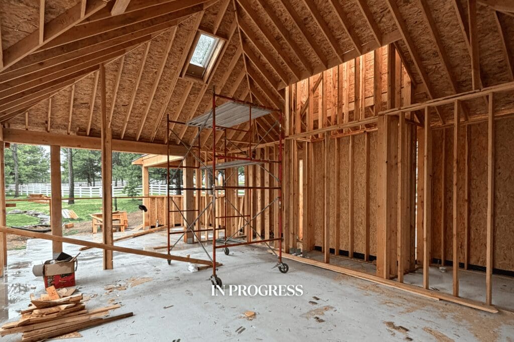 Construction progress of a Tulsa pool cabana renovation by Kirkendall Design showing interior framing for the fireplace, kitchen, and outdoor gathering space.