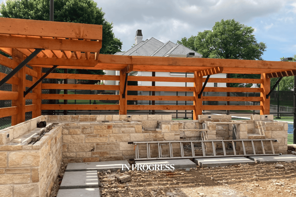 Construction progress of a Kirkendall Design outdoor kitchen in Tulsa, Oklahoma showing brick installation, pergola structure, and backyard renovation details.